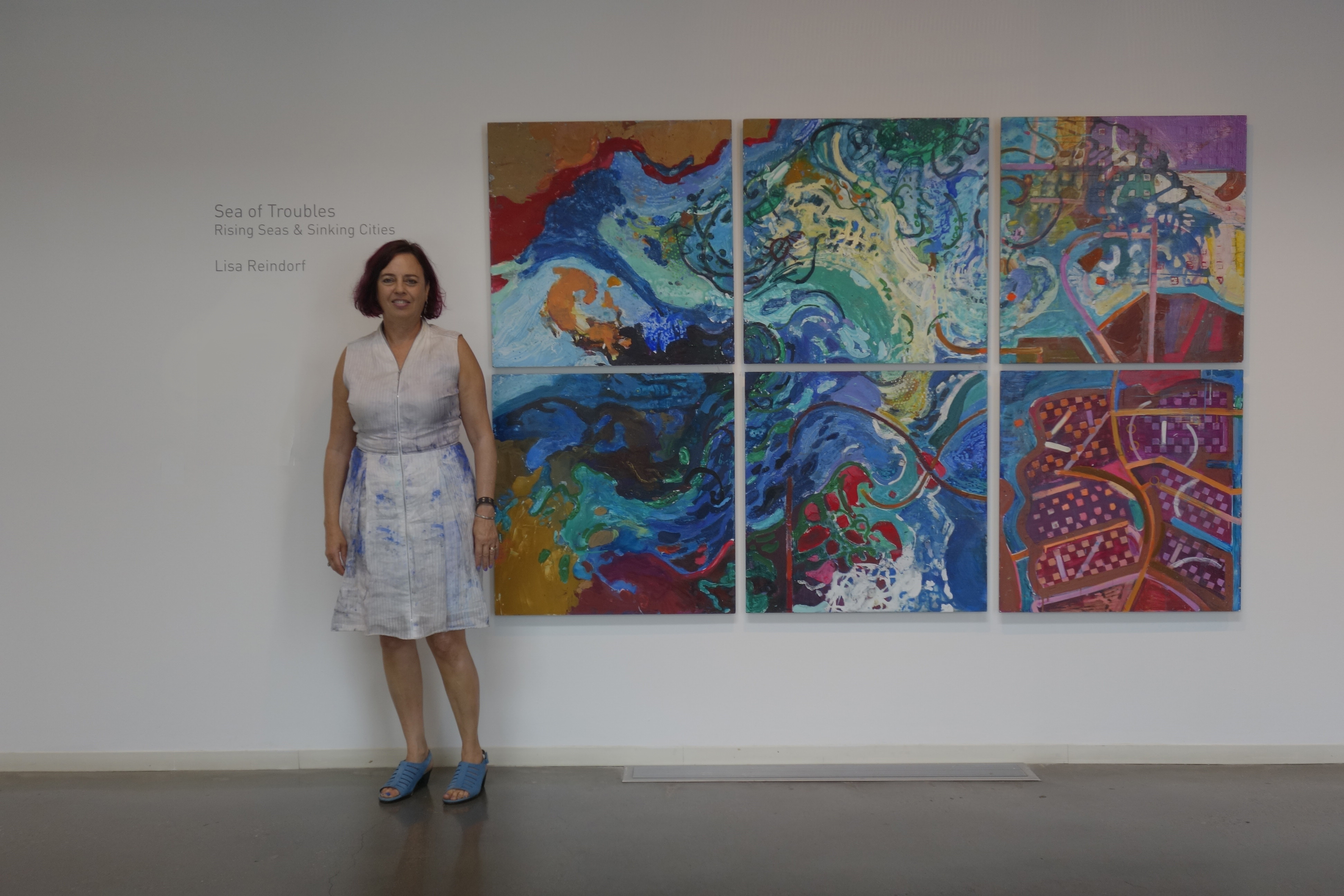 A woman standing in front of six paintings.