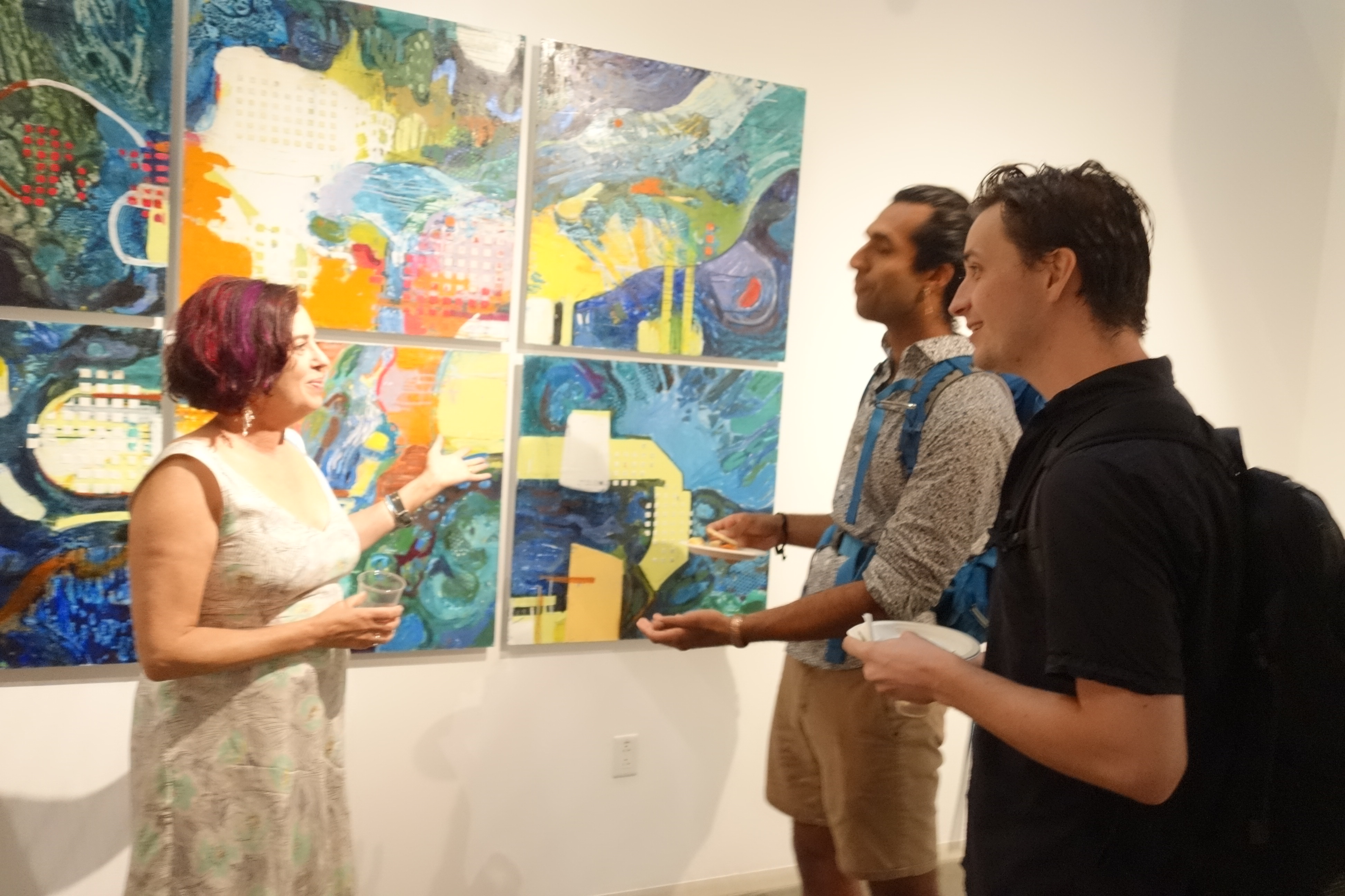 A group of people standing around in front of paintings.